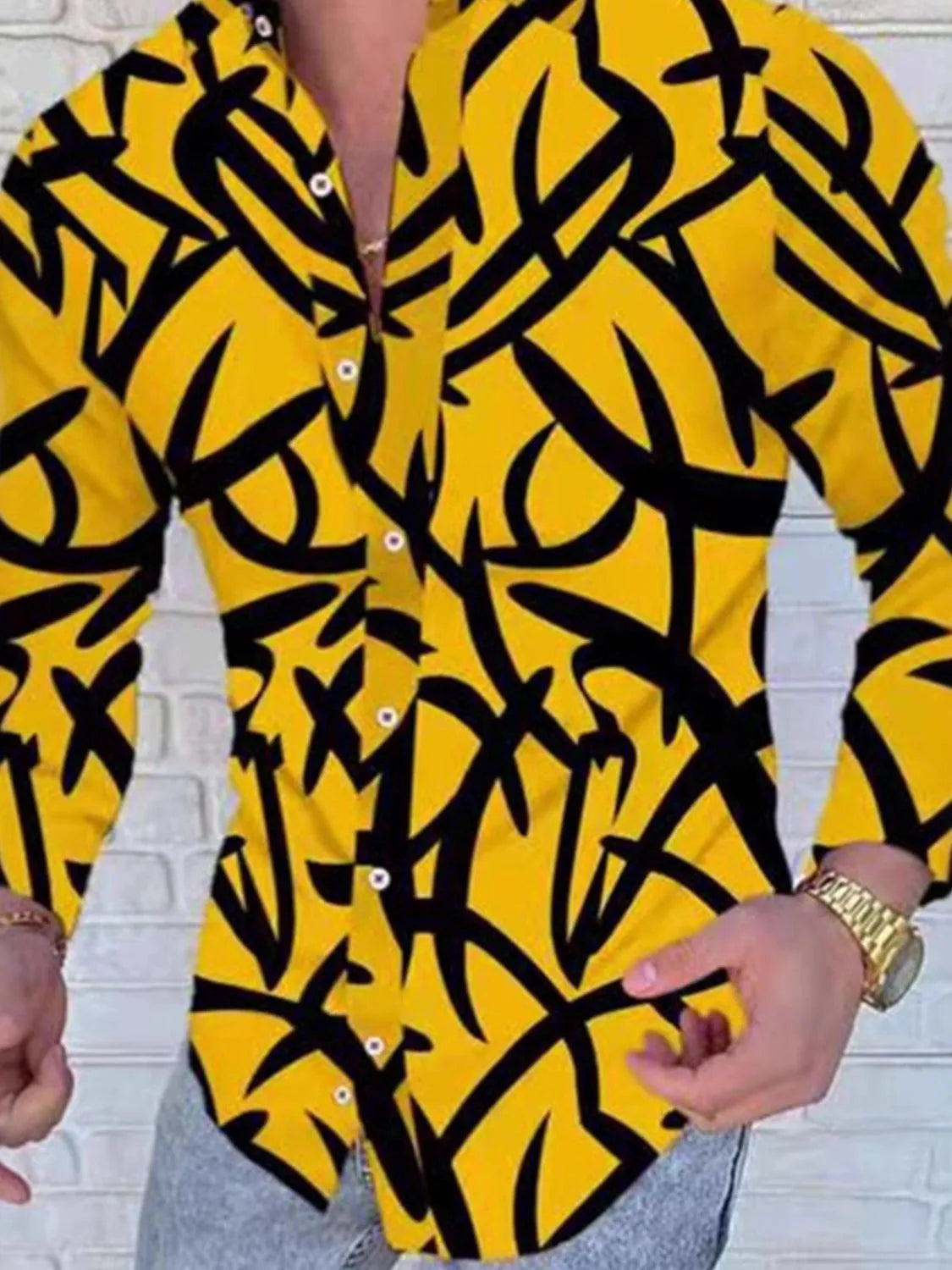 Yellow shirt with black abstract pattern worn by a person against a white brick wall.