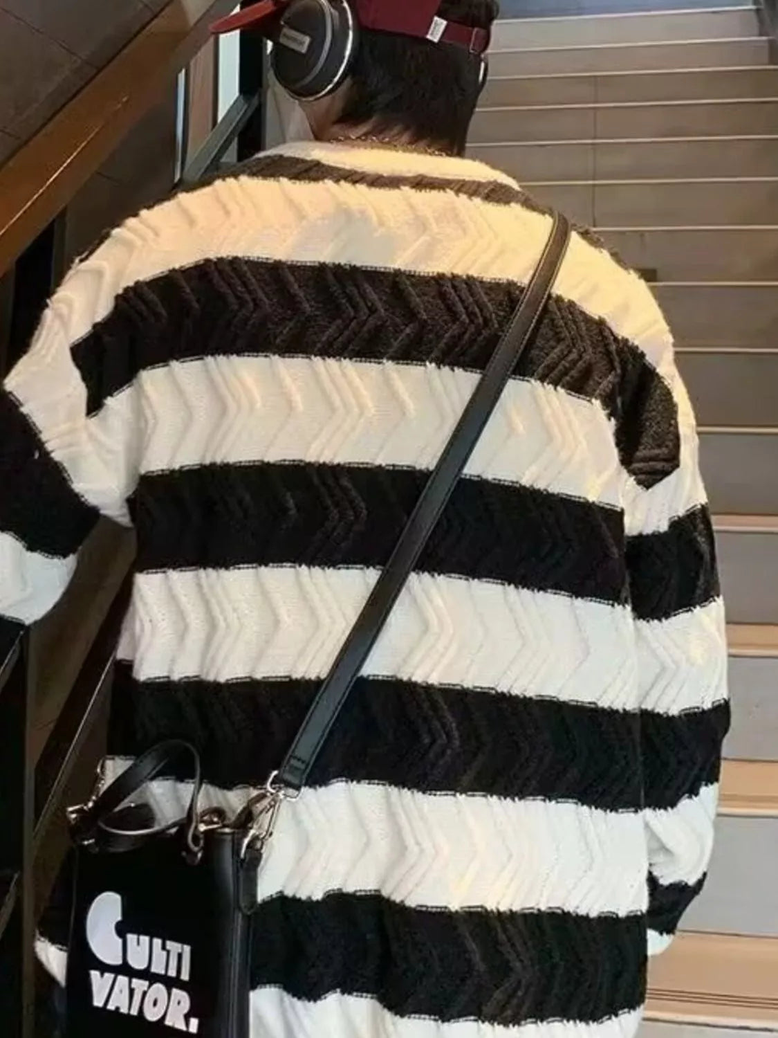 Person wearing a black and white striped sweater with a black bag, standing on stairs.