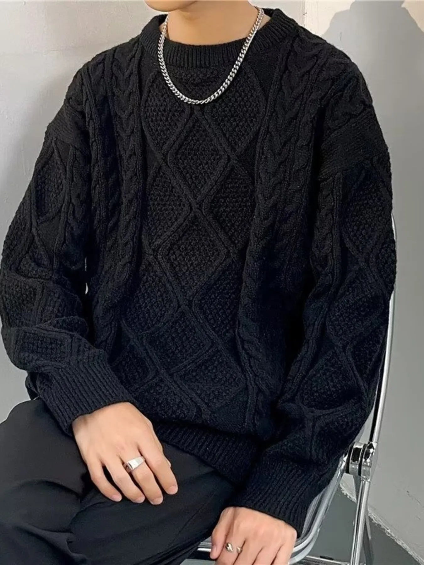Person wearing a black cable knit sweater sitting on a chair.