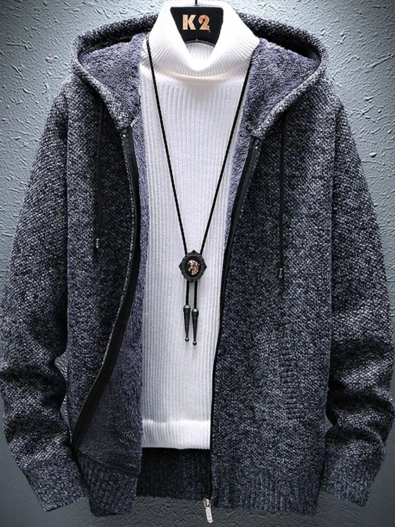 Gray hooded jacket over a white turtleneck with a necklace on a gray background