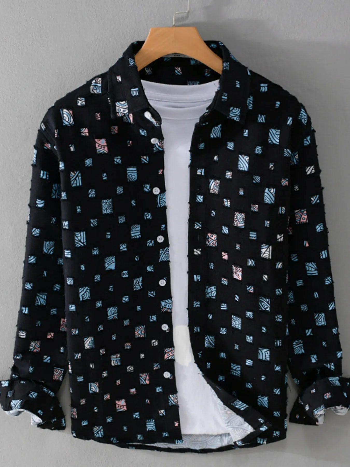 Black patterned shirt over a white t-shirt on a hanger against a gray background