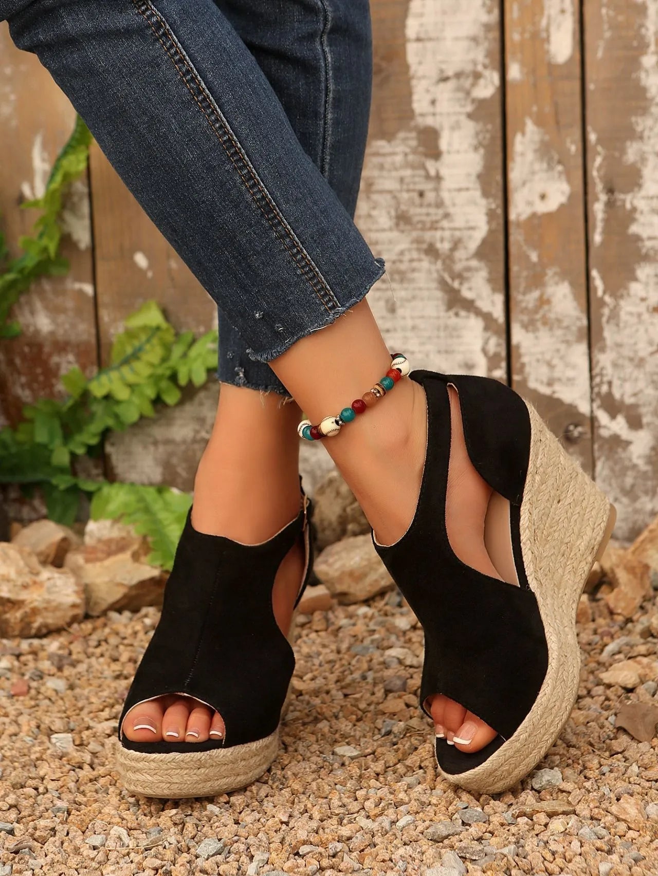Black wedge sandals worn with rolled-up jeans on a rustic background
