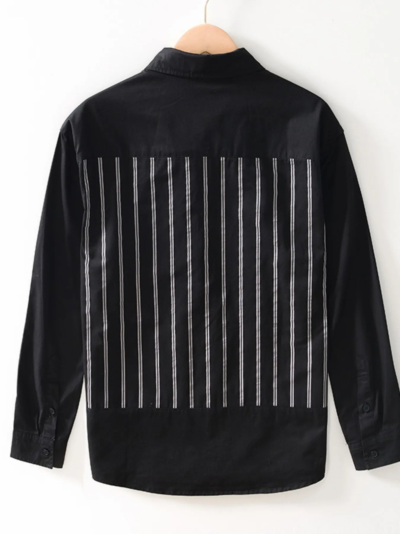 Black shirt with white vertical stripes on a hanger against a white background