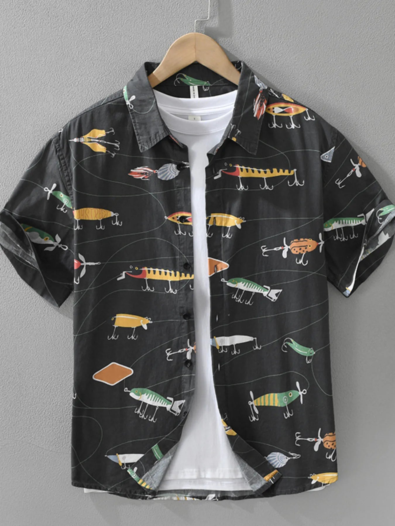 Black shirt with colorful fishing lure pattern on a hanger against a gray background