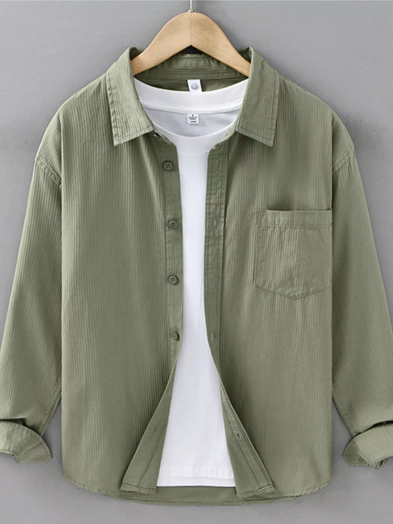 Green shirt over a white t-shirt on a hanger against a gray background