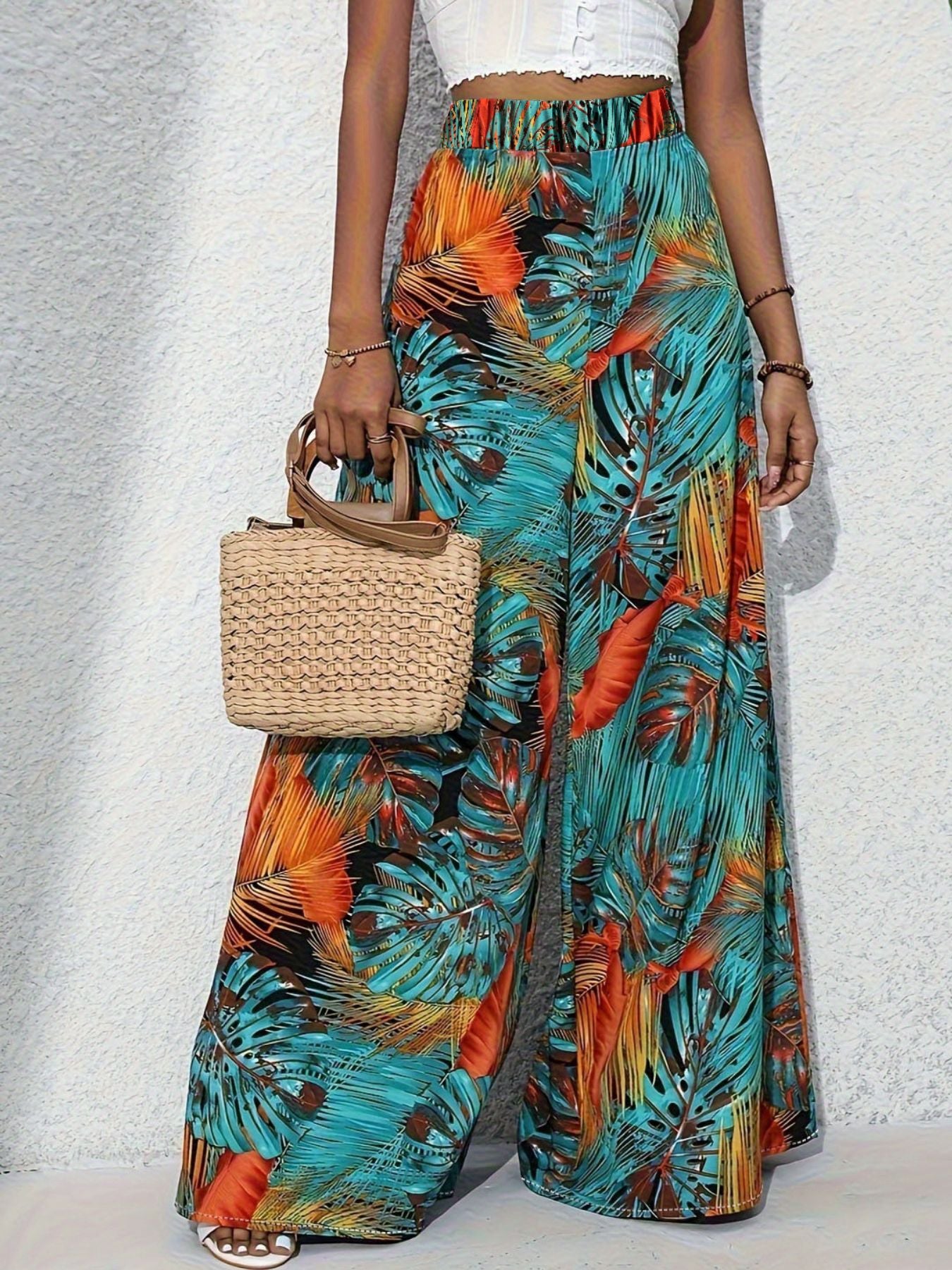 Person wearing colorful tropical print pants holding a woven bag on a light gray background