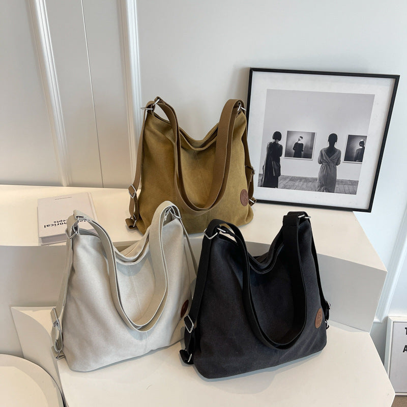 Three handbags in gray, black, and brown on a white surface with a framed picture in the background.