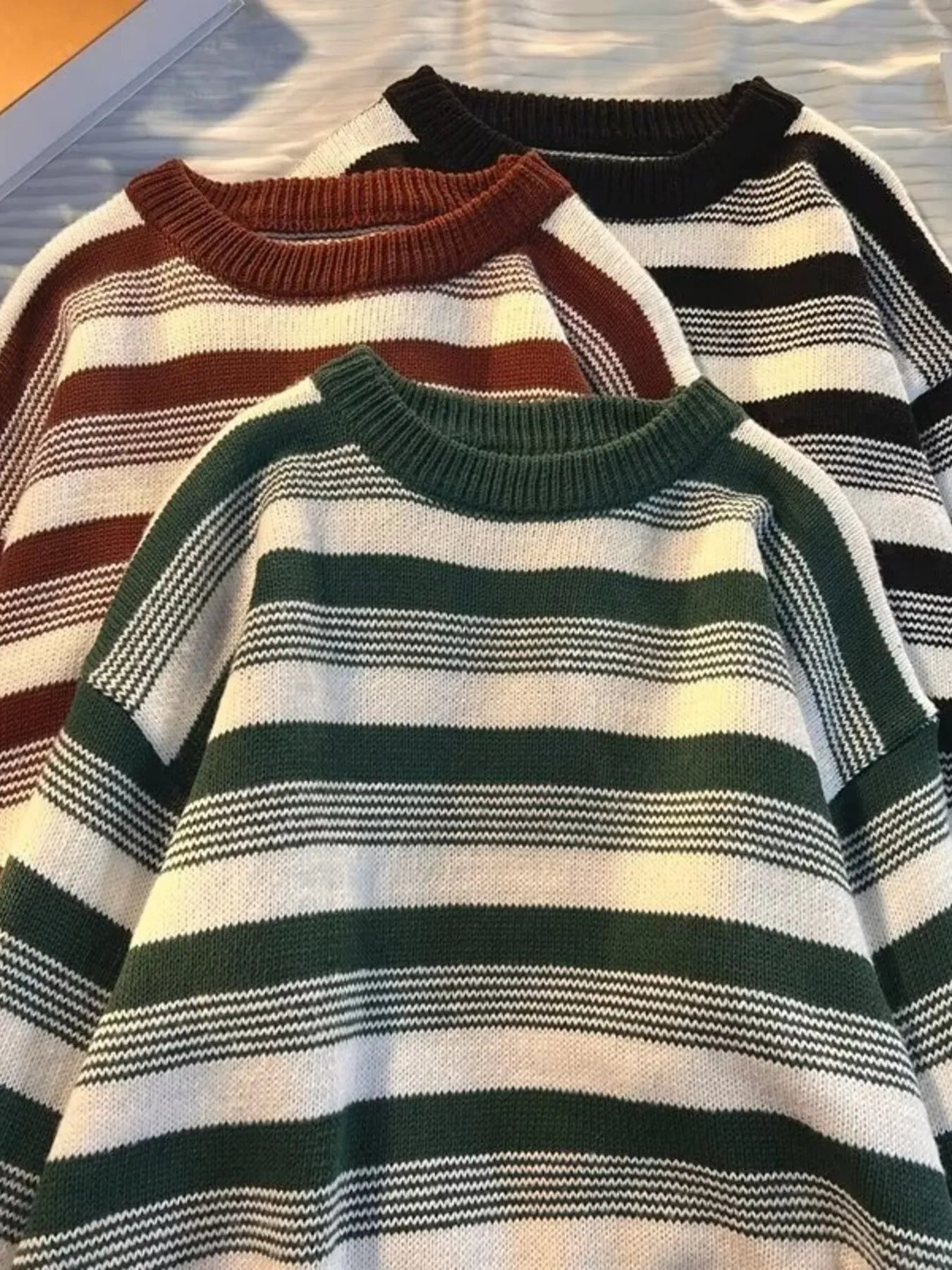Three striped sweaters in different colors on a textured surface.