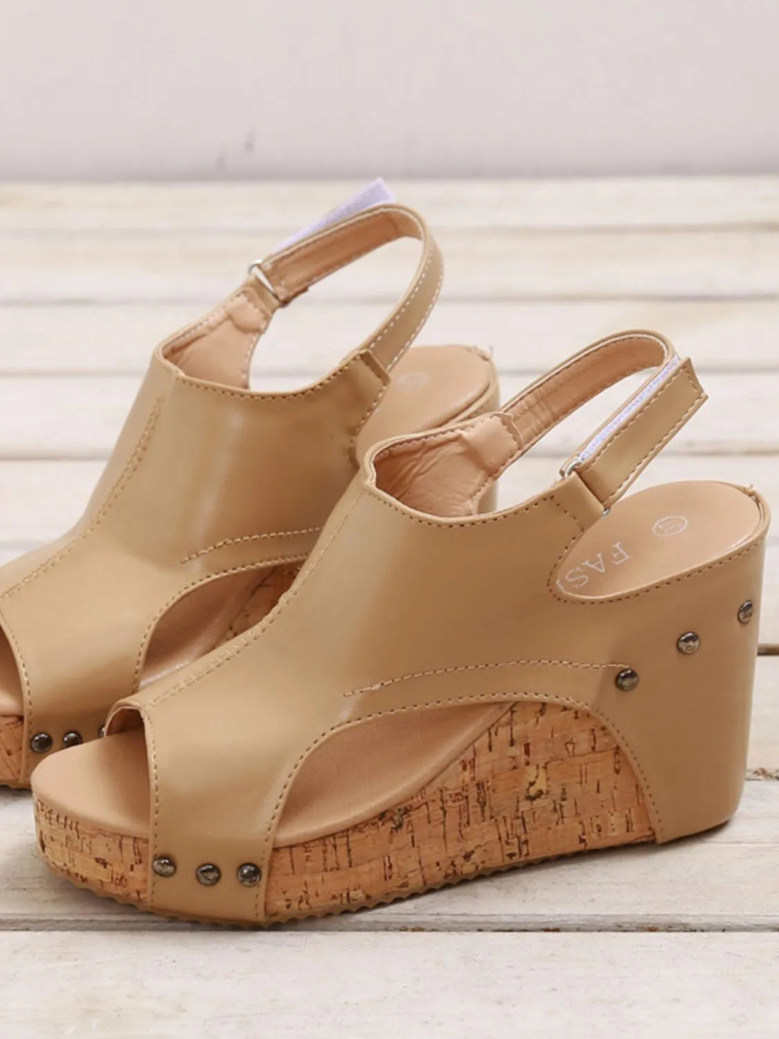 Beige wedge sandals with cork sole on a light wooden floor