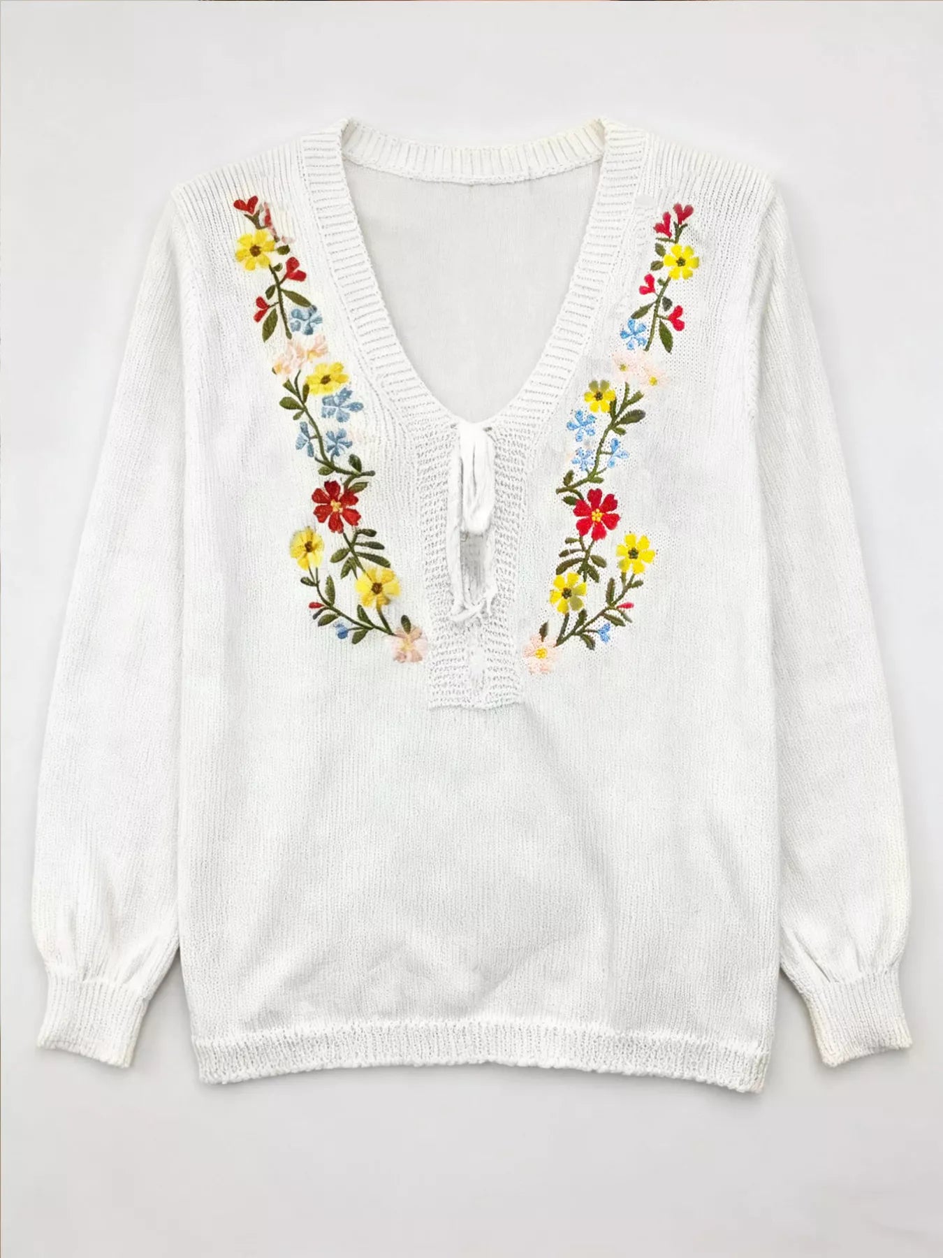 White sweater with colorful floral embroidery on a white background