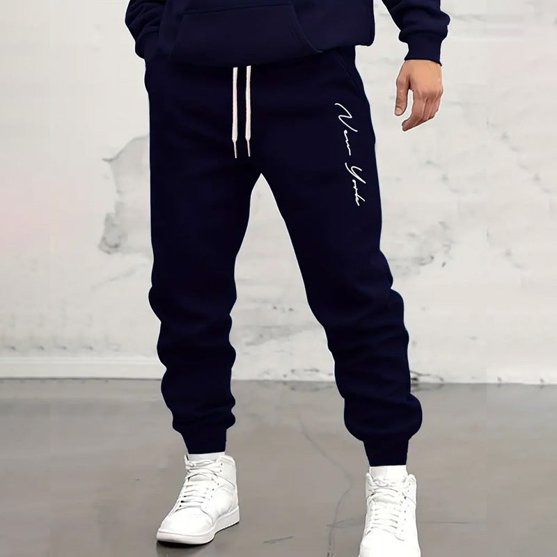 Navy blue jogger pants with white drawstring and 'New York' text, worn with white sneakers on a light gray background.
