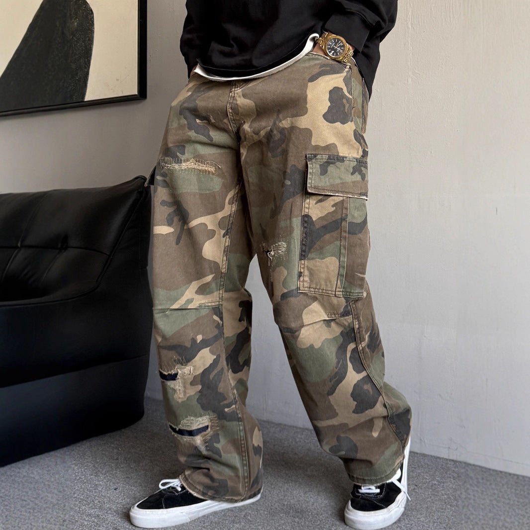 Person wearing camouflage pants and black sneakers in a room with a black bag and abstract art on the wall.