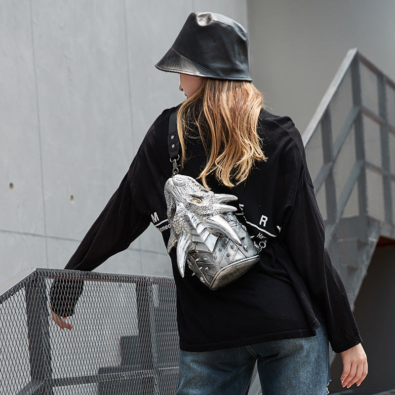 Person wearing a black jacket and silver backpack with a dragon design, standing against a gray wall.