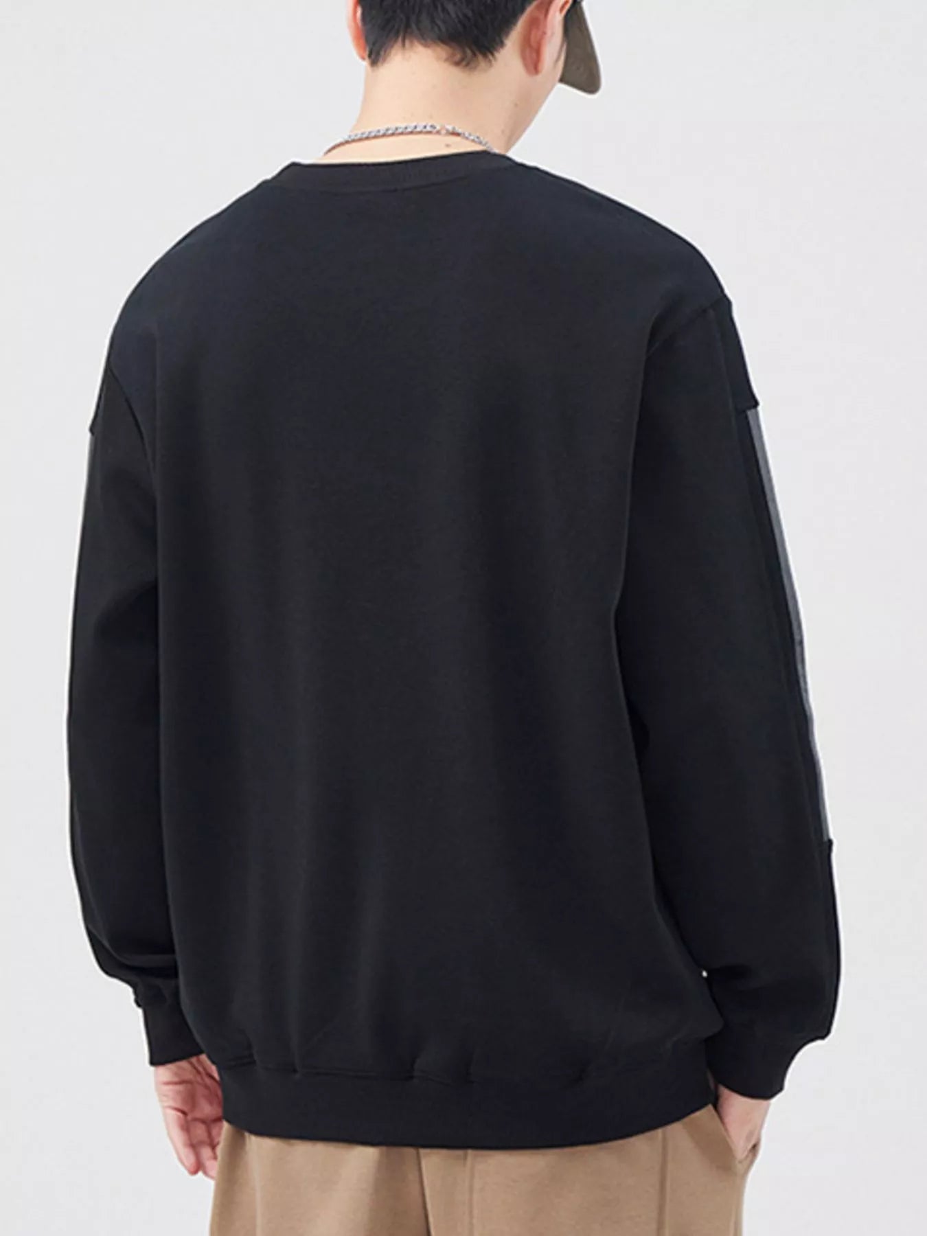 Person wearing a black sweatshirt with beige pants on a white background
