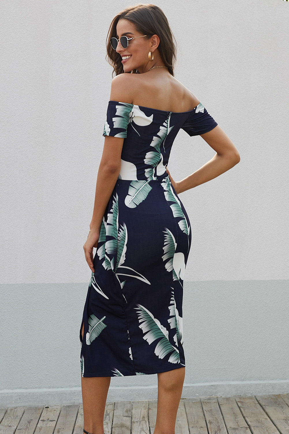 Woman wearing a navy off-shoulder dress with tropical leaf pattern against a light gray background.