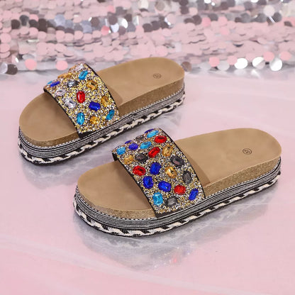 Decorative sandals with gemstones worn by a person on a glittery background