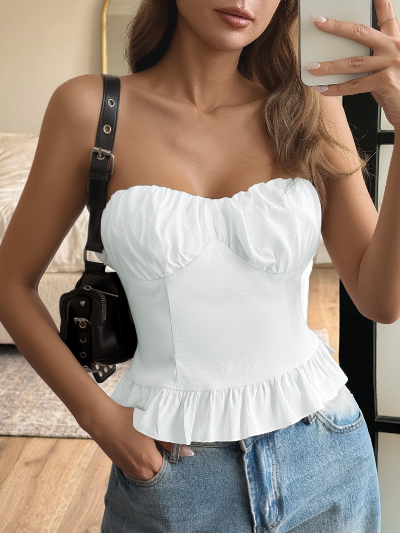 Woman wearing a white ruffled top and blue jeans, holding a phone.