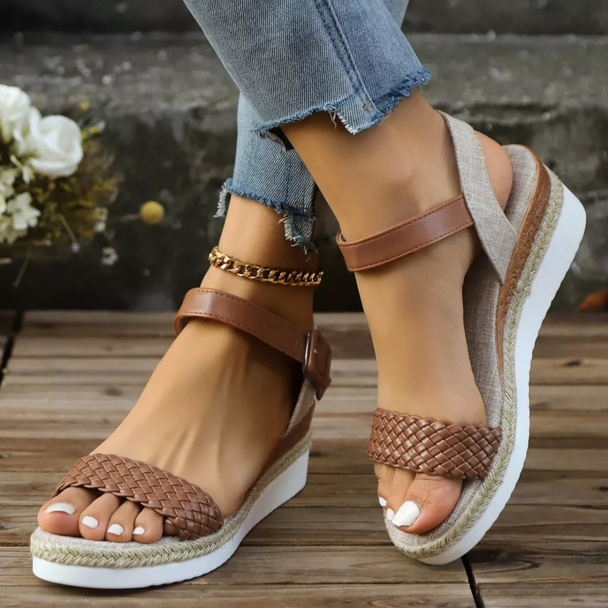 Brown wedge sandals with braided details worn with denim jeans on a wooden floor.