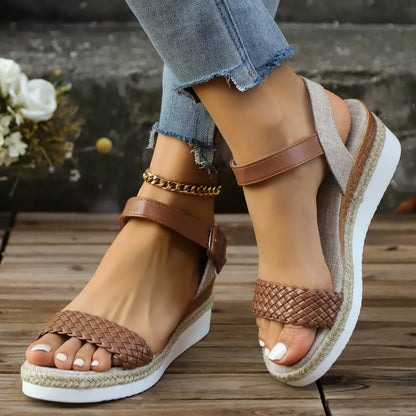Brown wedge sandals with braided details worn with denim jeans on a wooden floor.