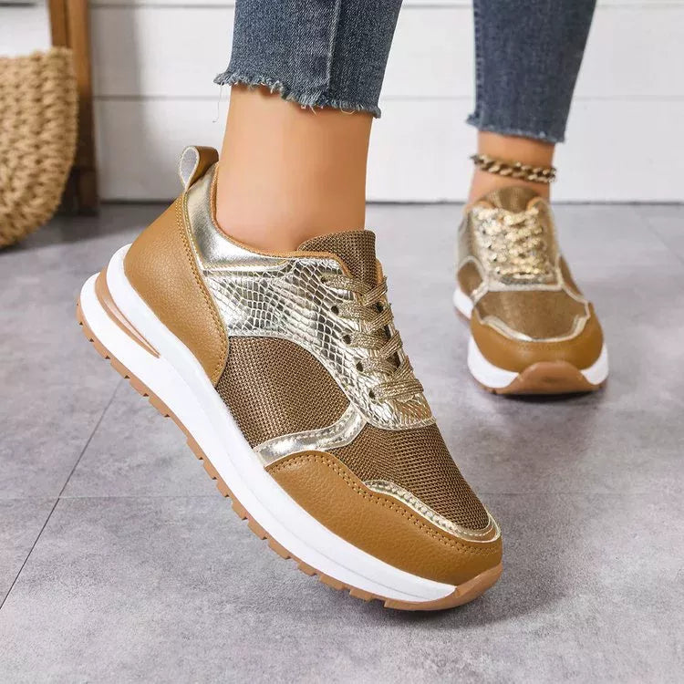 Brown and gold sneakers worn with jeans on a gray floor.