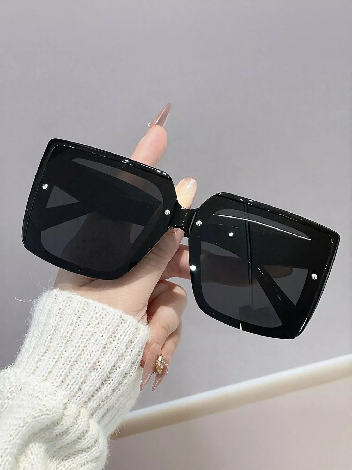 Black sunglasses held by a hand against a gray background