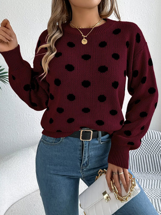 Person wearing a burgundy sweater with black polka dots and blue jeans, holding a white handbag.