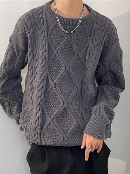 Person wearing a gray cable knit sweater against a plain background