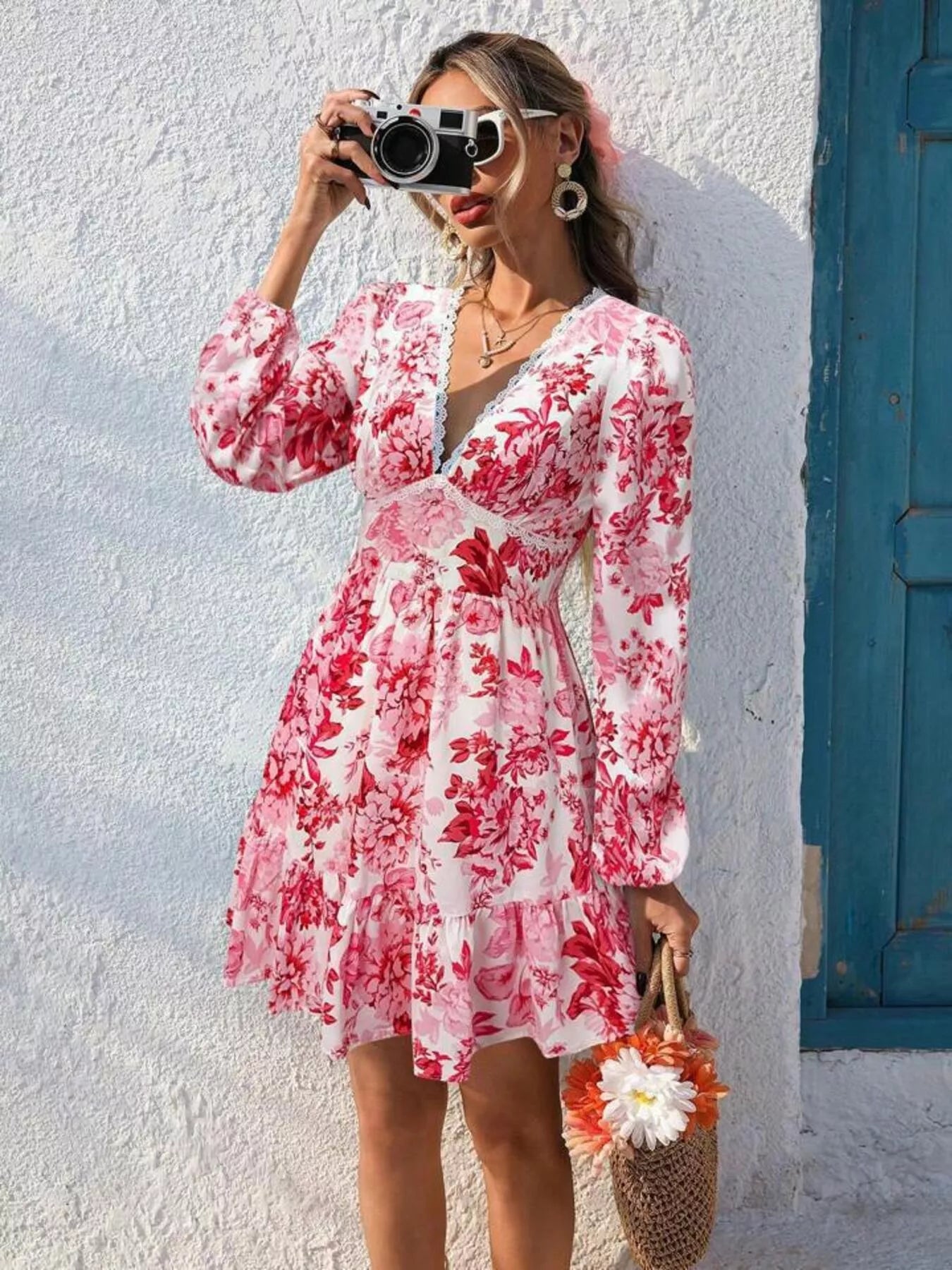 Woman in a pink floral dress taking a selfie against a white wall with a blue door.