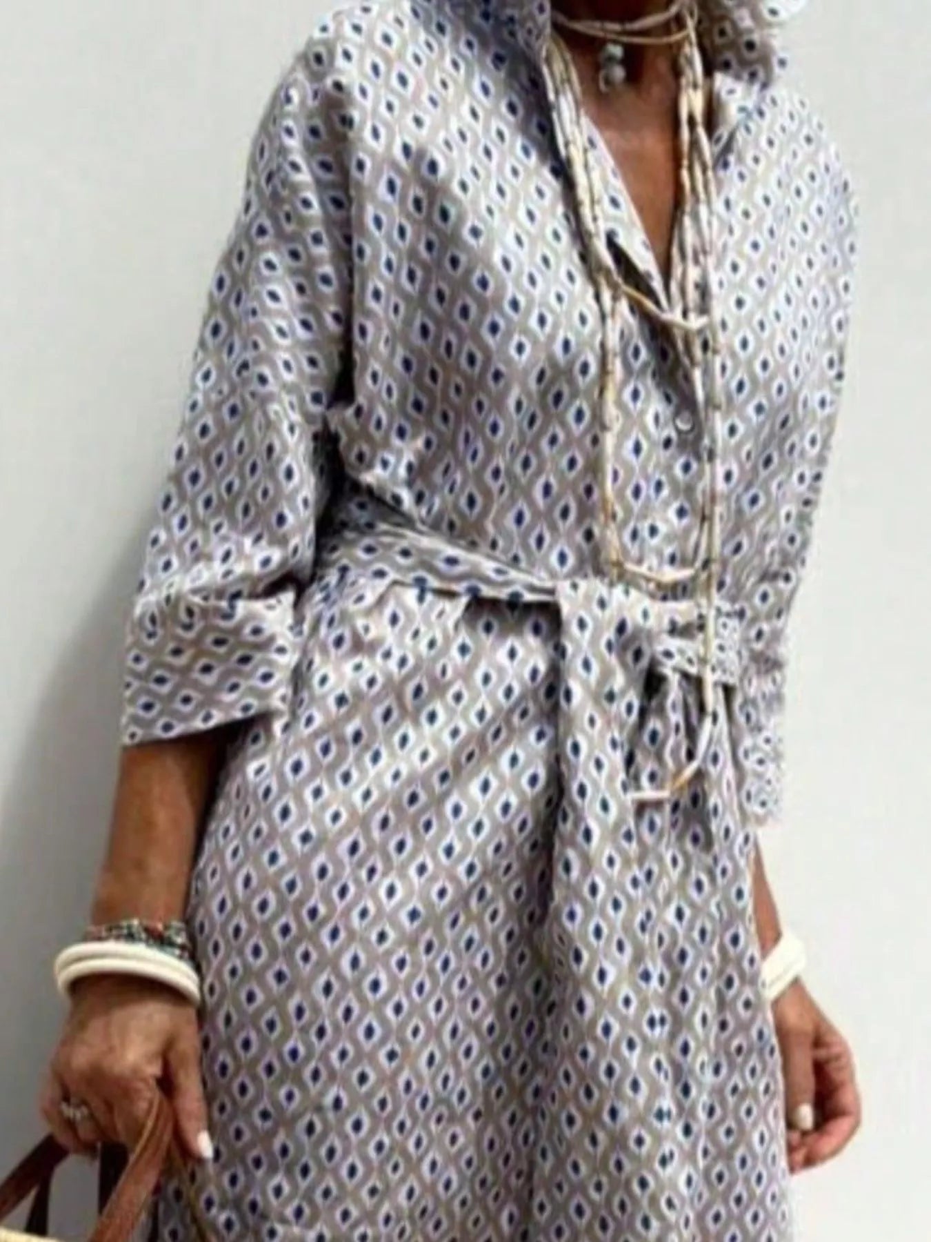 Person wearing a patterned dress with a belt against a plain background
