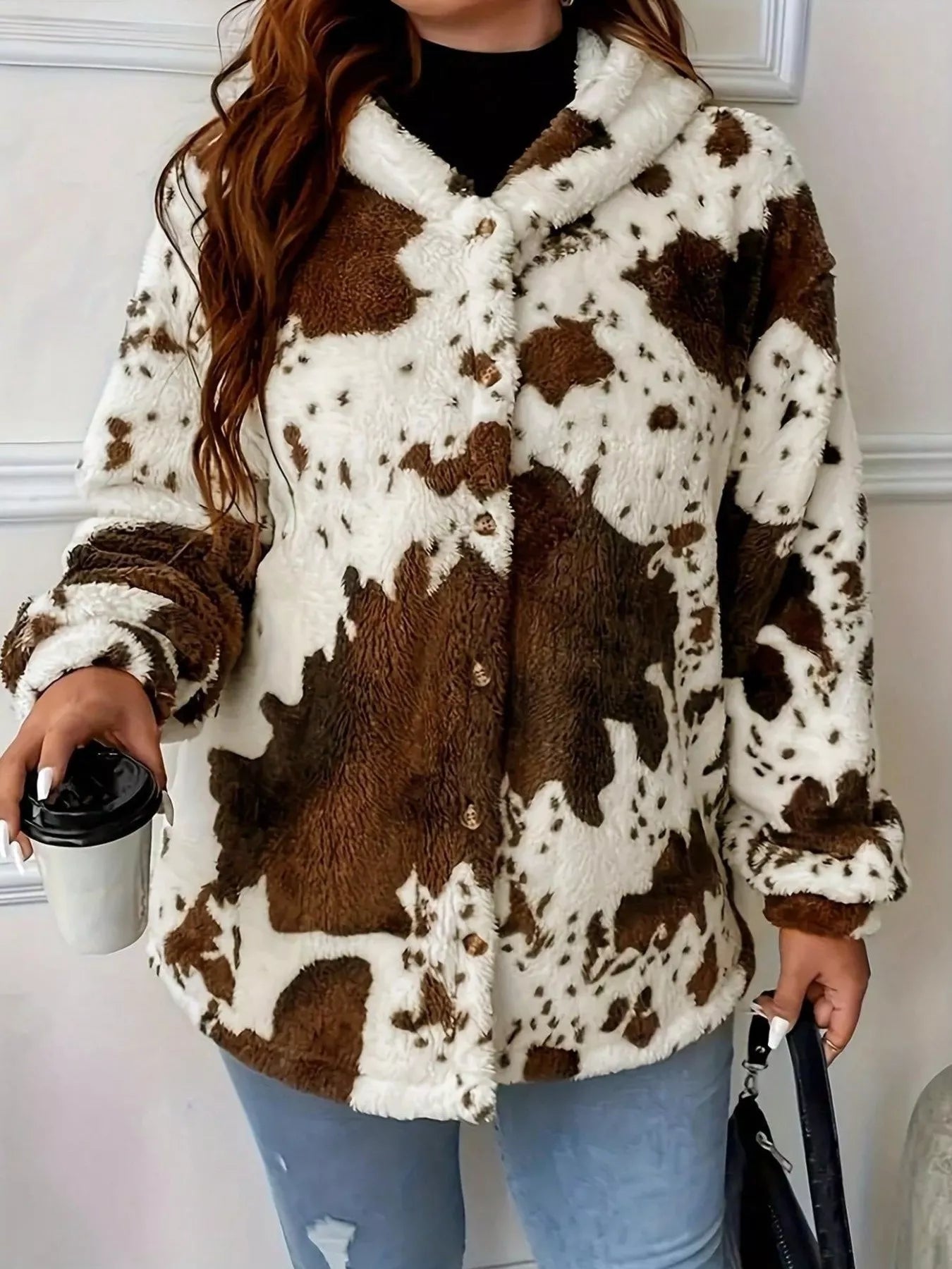 Person wearing a brown and white cow print jacket holding a black coffee cup.