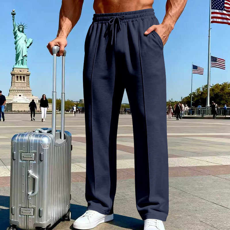 Person wearing navy pants with a silver suitcase in front of the Statue of Liberty.