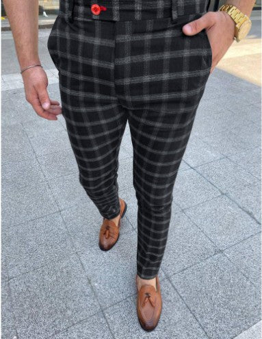 Person wearing black and gray plaid pants with brown shoes on a pavement background
