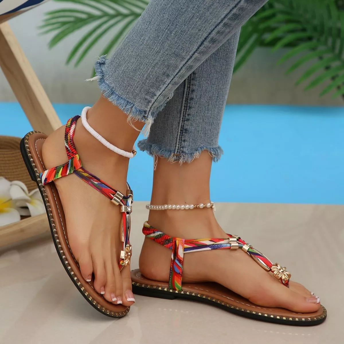 Colorful sandals with decorative straps worn by a person sitting by a pool.