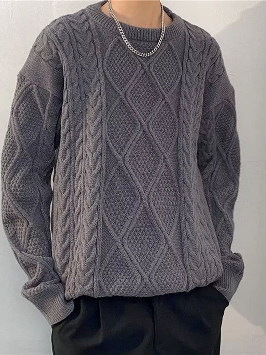 Person wearing a gray cable knit sweater against a plain background