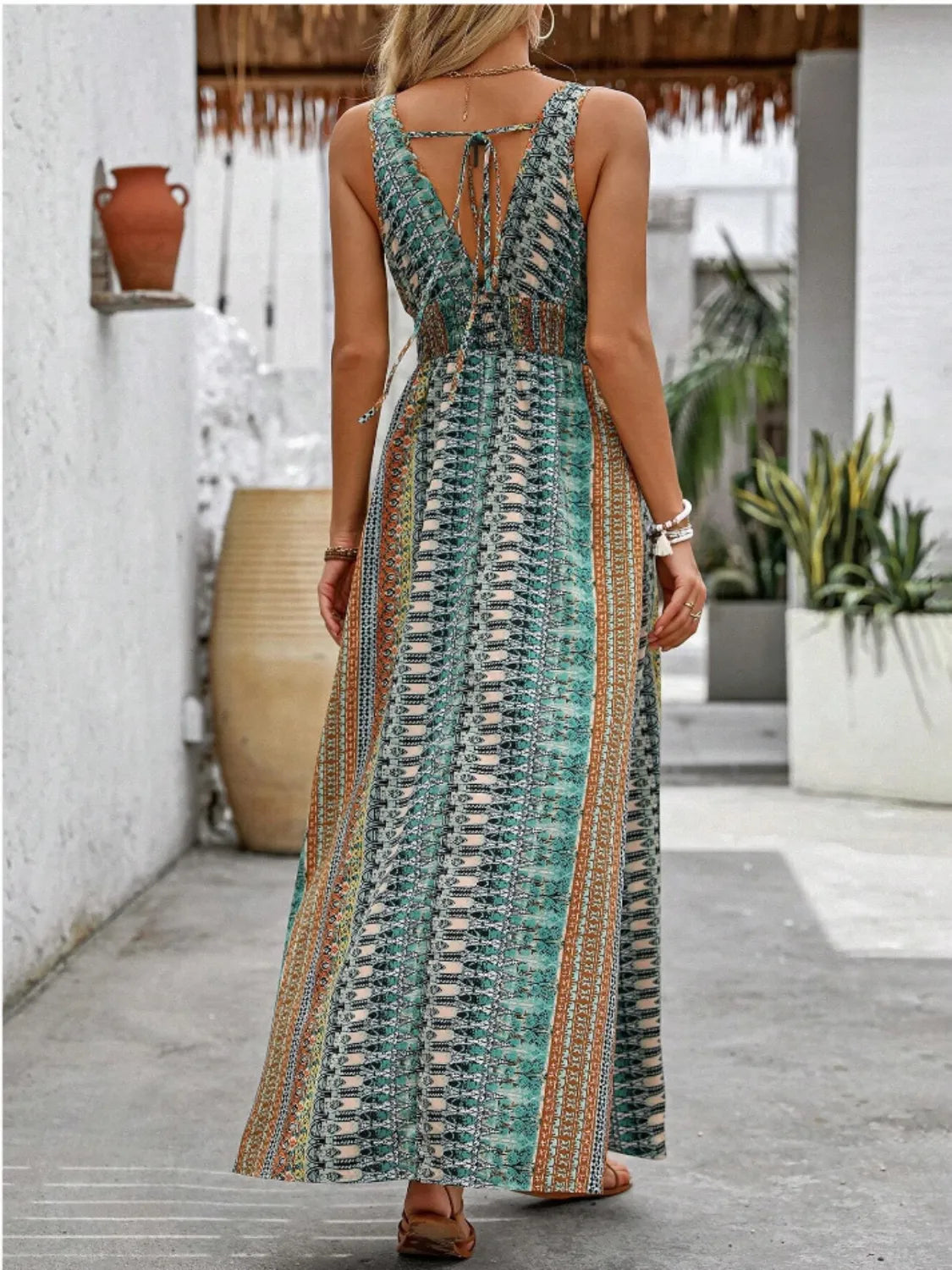 Woman wearing a long, patterned dress with a white wall and plants in the background
