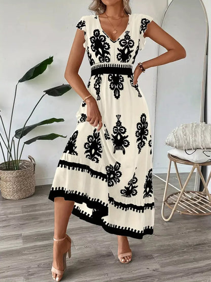 Woman wearing a white dress with black floral patterns in a room with a plant and chair.