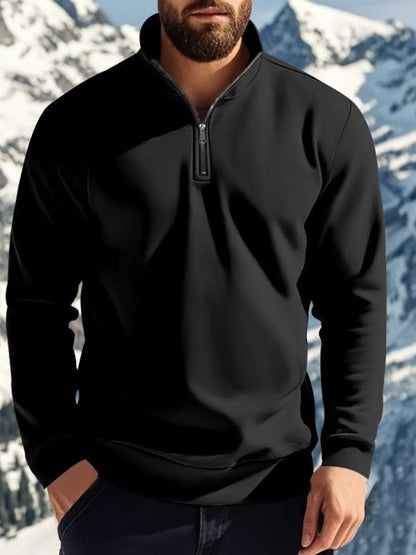 Person wearing a black quarter-zip sweatshirt with a mountainous background
