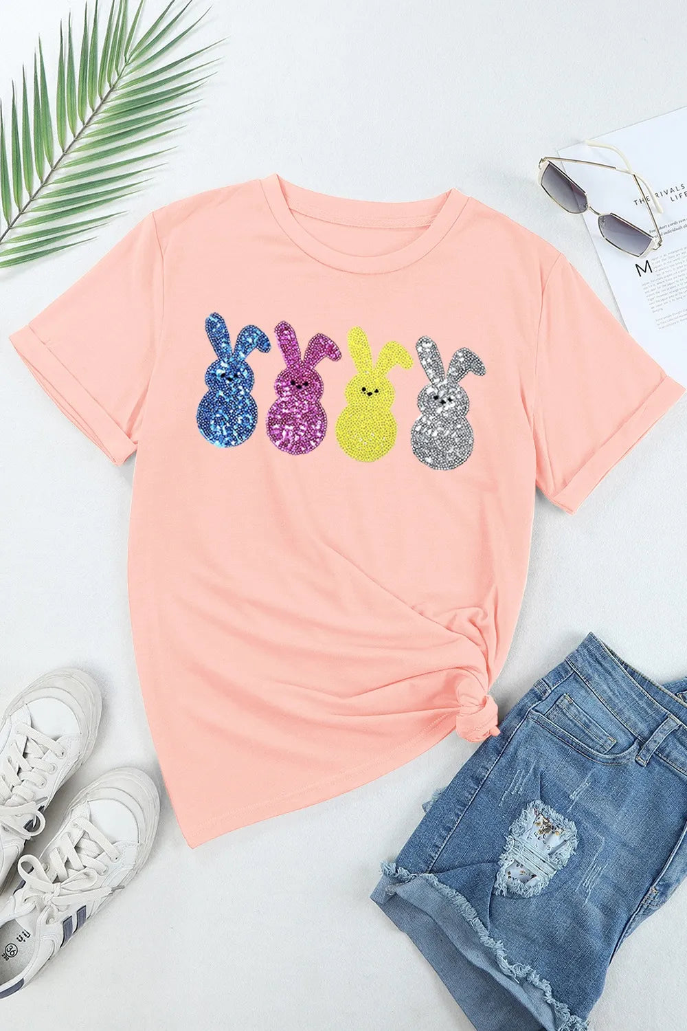 Pink t-shirt with colorful bunny graphic, sunglasses, and shorts on a light background