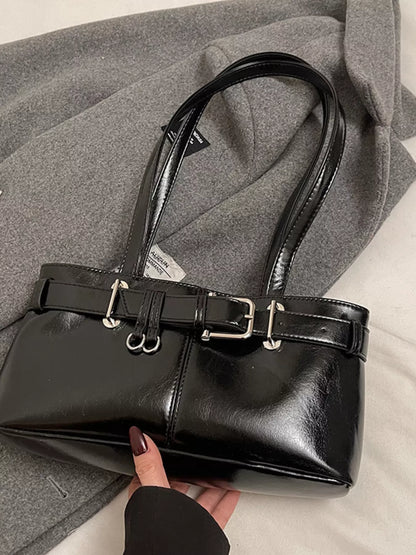 Black handbag with a belt detail held by a hand against a gray coat background