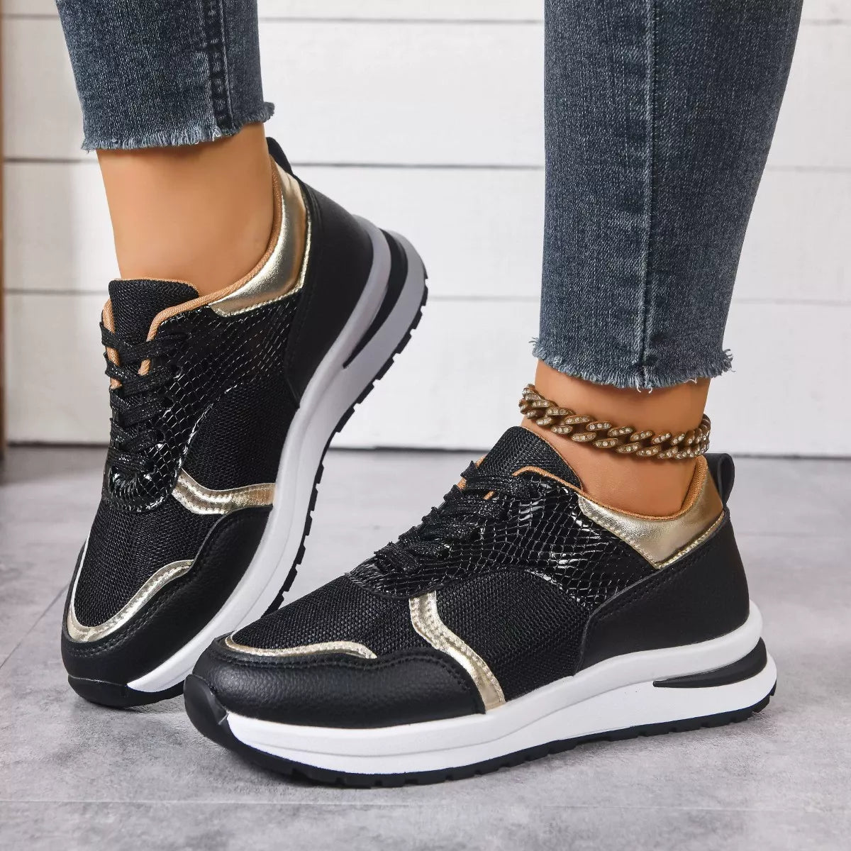 Black and gold sneakers worn with jeans on a light background