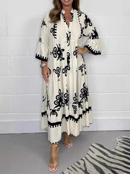 Woman wearing a white dress with black patterns against a white brick wall.