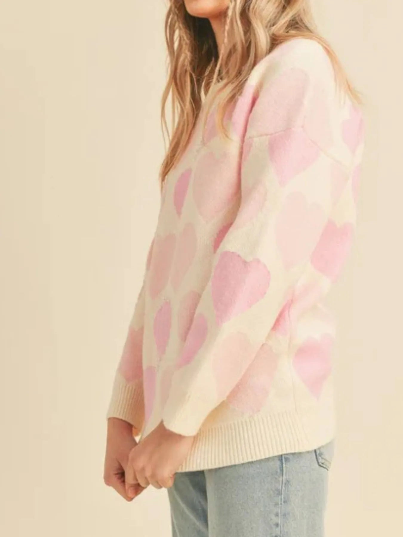 Person wearing a pink heart-patterned sweater against a beige background