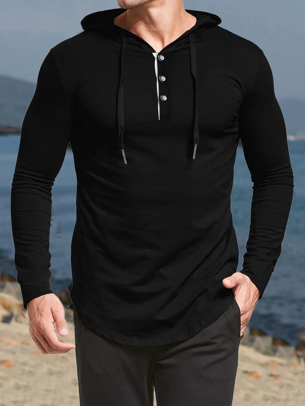 Person wearing a black long-sleeve hoodie with buttons by the ocean.