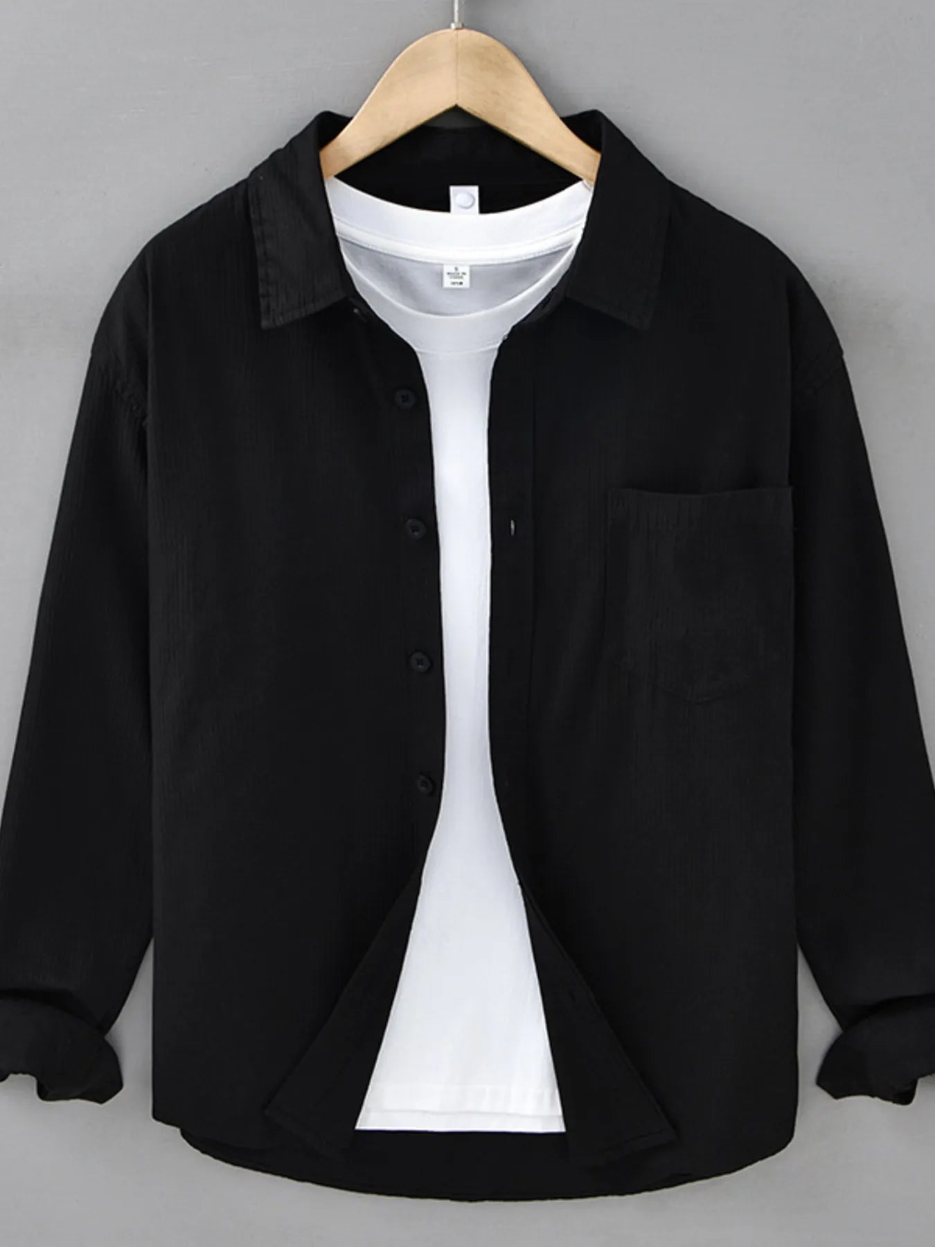 Black shirt over a white shirt on a hanger against a gray background