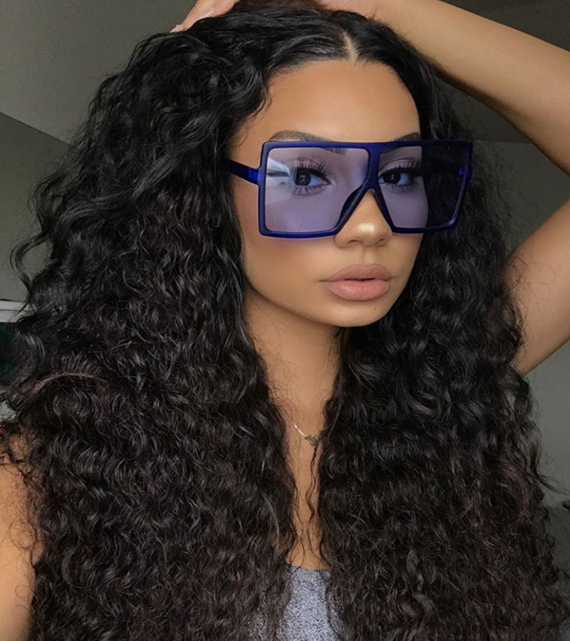 Person with long curly hair wearing large blue sunglasses indoors.