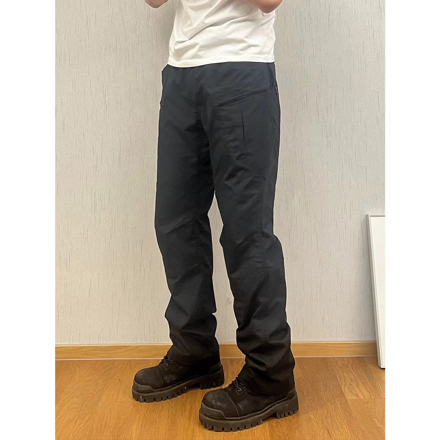 Person wearing dark pants and black boots standing against a light-colored wall.