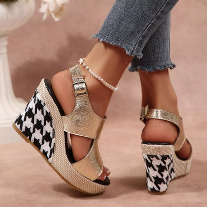 Gold wedge sandals with houndstooth pattern worn by a person, with a blurred floral 