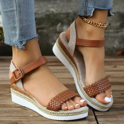 Brown wedge sandals with braided details worn by a person on a wooden floor.