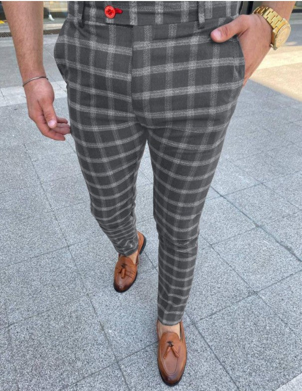 Person wearing gray plaid pants and brown shoes on a pavement.