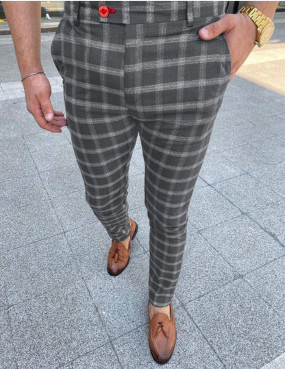 Person wearing gray plaid pants and brown shoes on a pavement.